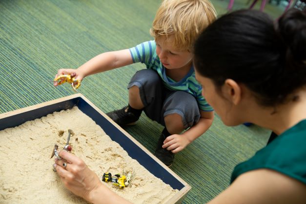 Play therapist and young child storytelling in the sand tray with symbols. 